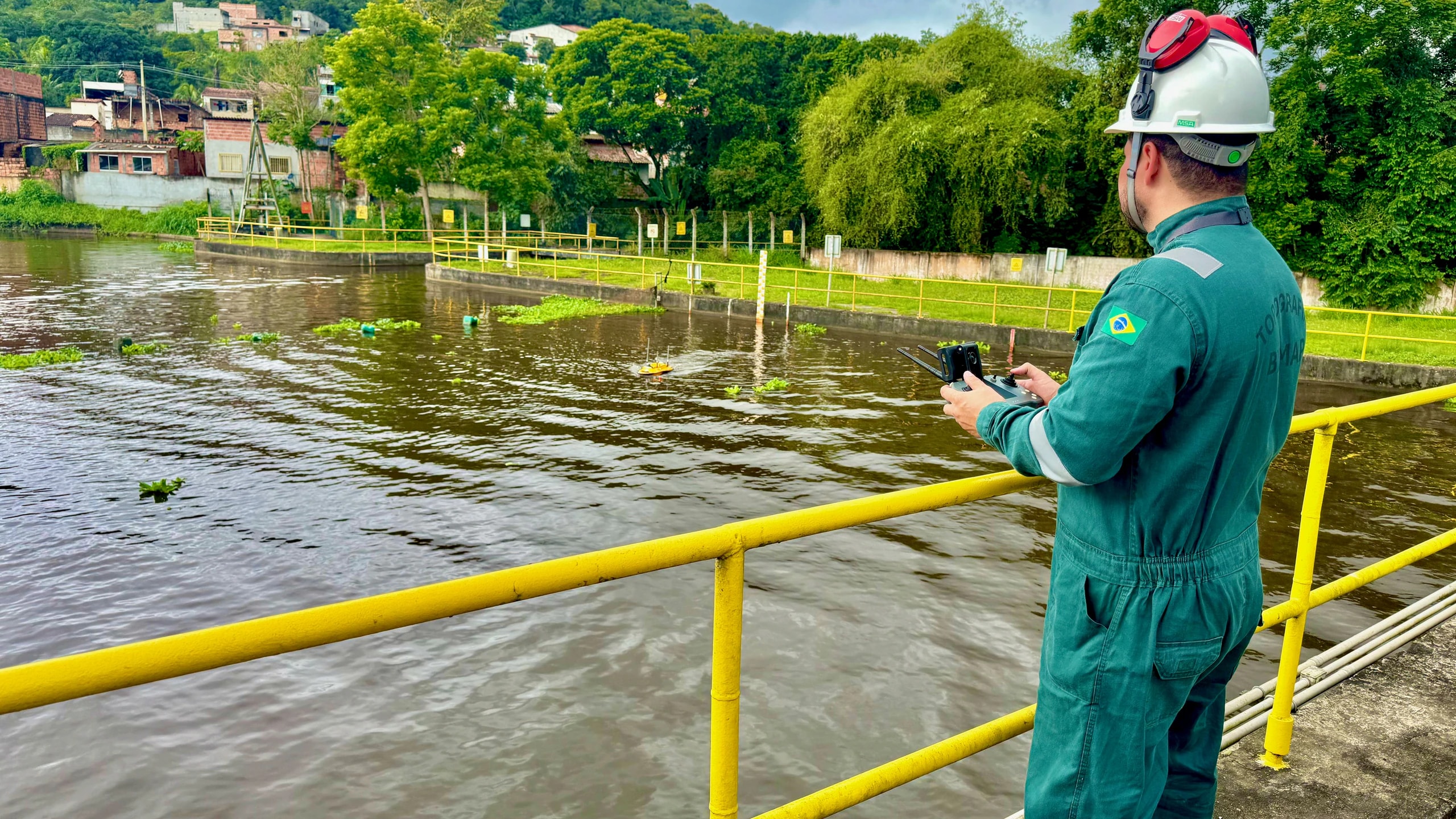 Operador BIOMAP no guarda-corpo sobre rio urbano, controlando o USV