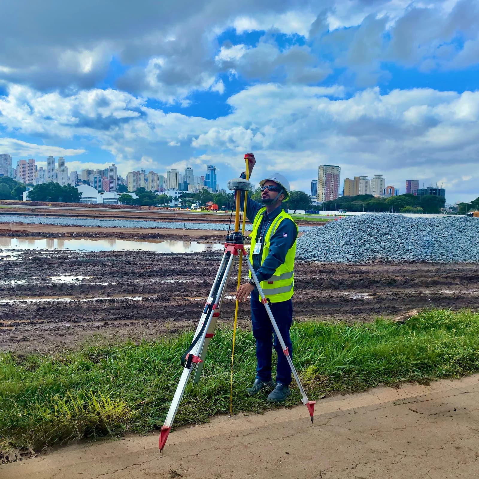Operador BIOMAP com nível em tripé, orla e cidade ao fundo